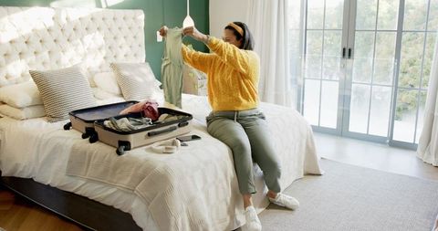 Woman organizing clothes for relaxing getaway in sunlit bedroom