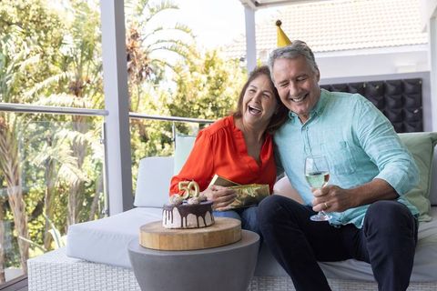 Mature couple celebrating 50th birthday on veranda with chocolate cake and wine