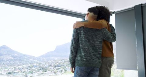 Friends embracing while looking at scenic city view through window