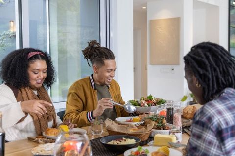 African american friends enjoying casual home dinner with man serving large fresh salad