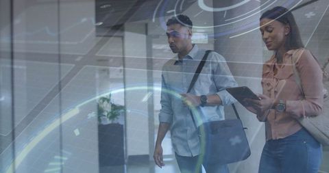 Walking business colleagues analyzing virtual technology in modern office hallway