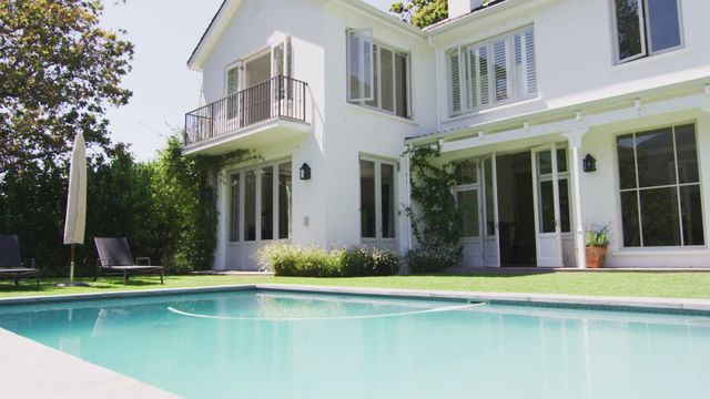 Elegant white house with a pool in the backyard. Perfect for real estate ads, vacation rentals, and home improvement projects. The sunny day and lush green lawn create a modern and welcoming environment.