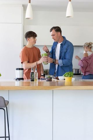 Modern family preparing healthy green smoothie together at bright kitchen island during morning