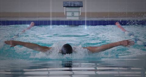 Competitive swimmer performing butterfly stroke in indoor pool lane with water splash