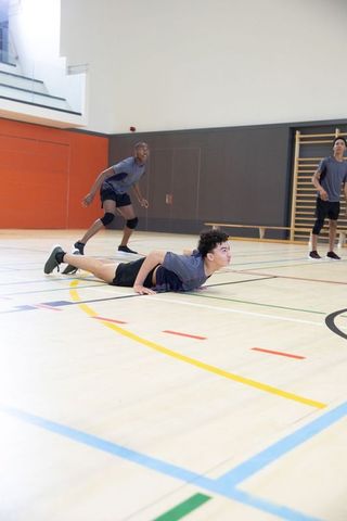 Teen athletes diving on indoor gym court during volleyball practice