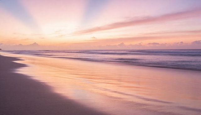 Pastel sunrise reflecting on wet sand creating mirror band along tranquil shoreline