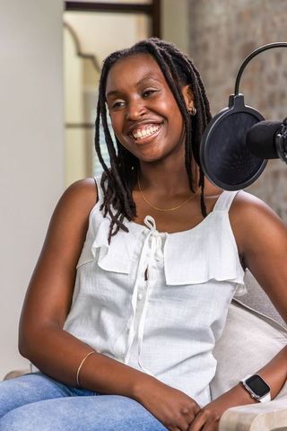 Smiling african woman speaking into microphone in cozy podcast studio armchair interview
