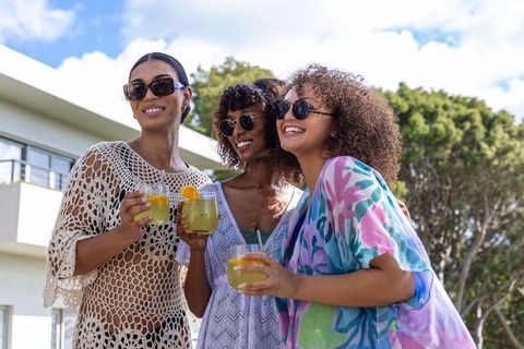 Three friends enjoying summer cocktails on balcony wearing bright cover-ups and sunglasses