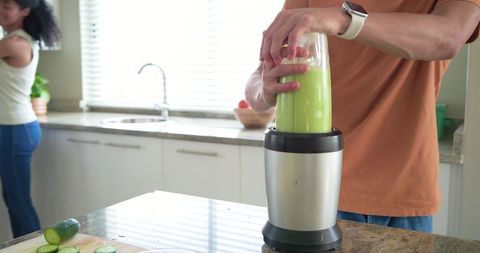 Diverse couple making green smoothie with blender on granite countertop at home kitchen