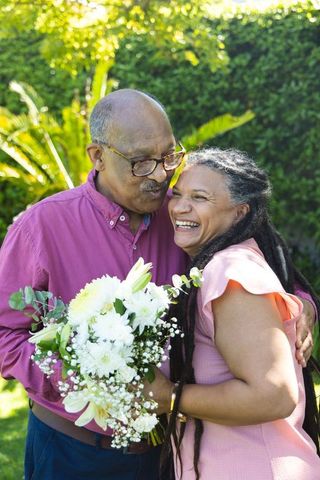 Mature african american couple laughing and embracing in sunlit garden with bouquet