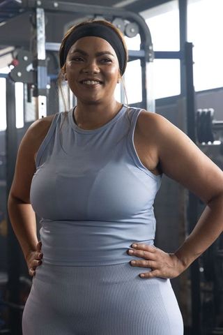 Confident african american woman standing in gym wearing light blue activewear smiling