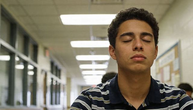 Teen student sitting with eyes closed in school hallway practicing mindfulness and calm