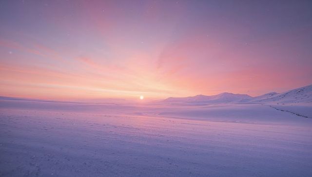 Sunrise bathing snowy tundra in pastel alpenglow with distant mountain ridge