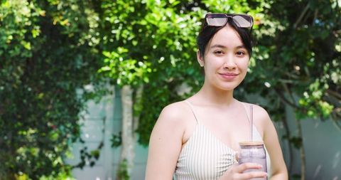 Asian Woman Holding Reusable Tumbler in Tranquil Backyard
