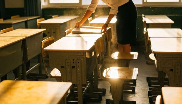 Teacher arranging sunlit classroom desks in golden dusty light calm morning