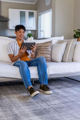 Young asian man relaxing on sofa using tablet in modern minimalist living room