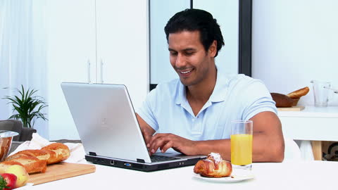 Man Typing on Laptop While Having Breakfast at Table