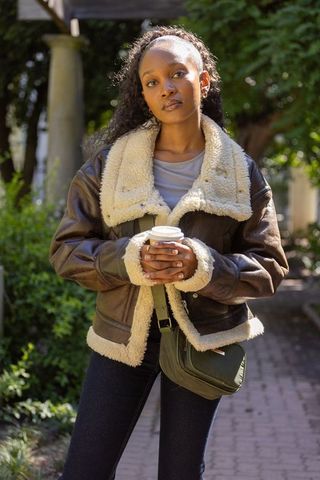 Sunlit portrait african american woman in shearling jacket holding coffee cup