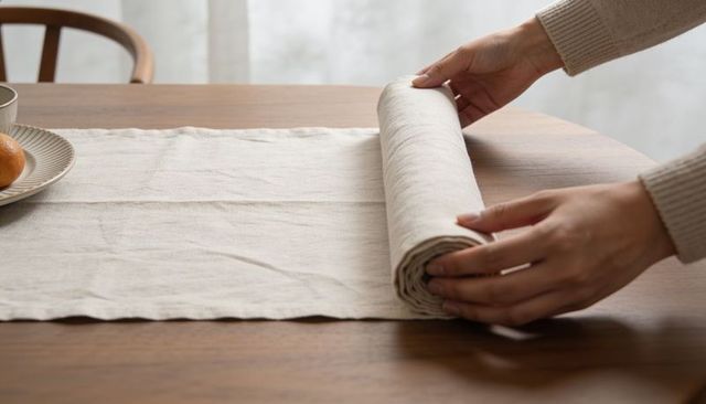 Hands rolling linen table runner on wooden dining table with neutral tableware