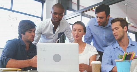 Collaborating team of five around laptop in modern sunlit office brainstorming ideas