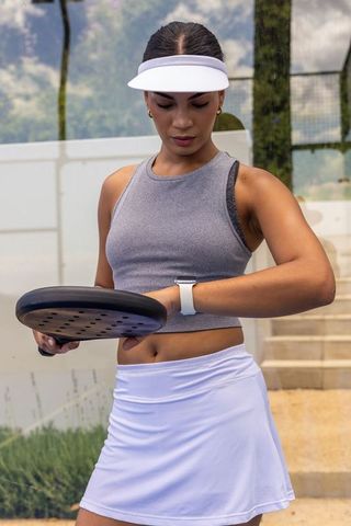 Athletic woman in white visor checking smartwatch while holding padel racket on outdoor court