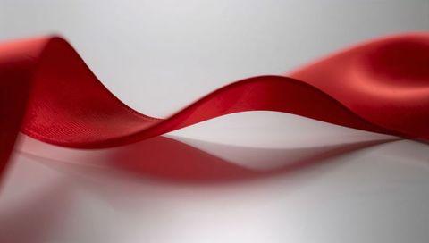 Curving red satin ribbon reflecting on glossy white surface, elegant silk wave with woven texture