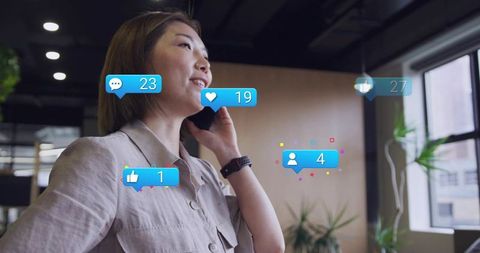 Asian businesswoman talking on phone in modern office with floating social media alerts