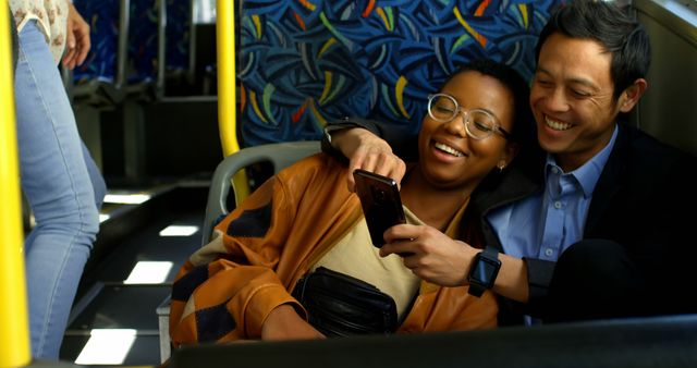 Happy diverse couple sitting in city bus embracing and using smartphone. Communication, transport, city living and lifestyle, unaltered.