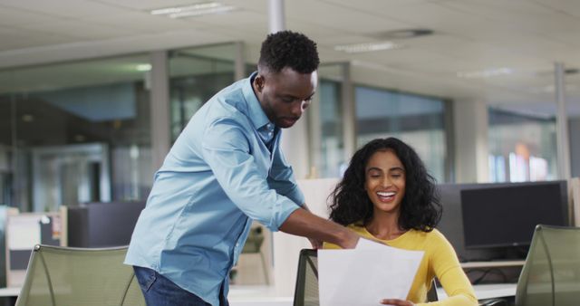 Young African business professionals collaborating in a modern office environment, with one person pointing at documents while the other smiles. Ideal for portraying productive workplace settings, teamwork, business projection scenarios, and office diversity.