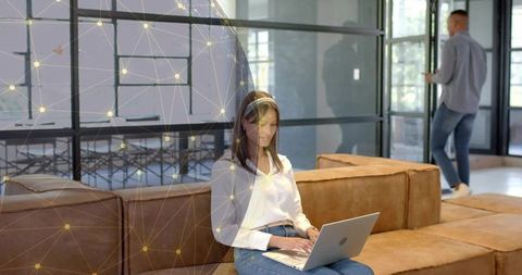 Woman working on laptop in modern coworking lounge wearing headset and casual jeans