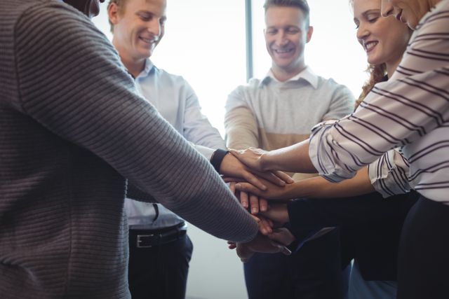Group of business colleagues stacking hands in office, showing unity and teamwork. Ideal for illustrating concepts of collaboration, team spirit, corporate culture, and successful partnerships in business environments.
