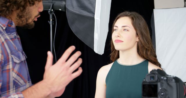 A Caucasian photographer is directing a young Caucasian woman during a studio photoshoot, with copy space. His guidance aims to capture her best angles while she poses with a subtle smile and focused gaze.