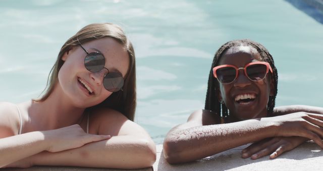 Happy diverse girls in sunglasses relaxing in swimming pool in the sun. Summer, vacations, friendship, fun and free time, unaltered.