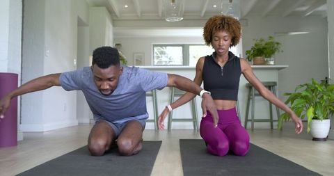 African american couple stretching together in sunlit modern kitchen wearing fitness trackers
