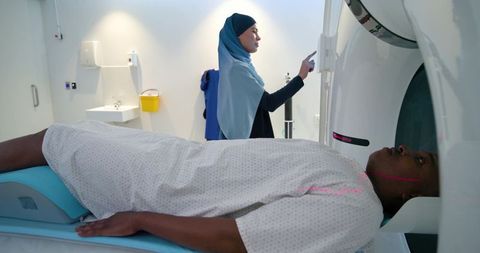 Muslim technologist operating ct scanner while african patient lying on gantry in hospital