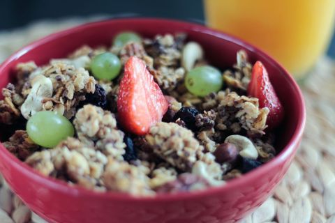 Red bowl featuring granola with strawberries, green grapes and nuts for healthy breakfast