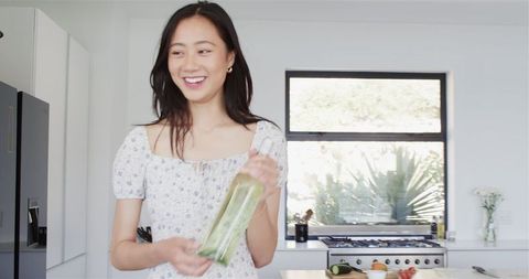Smiling Woman in Kitchen with Bottle Engages Friends at Party