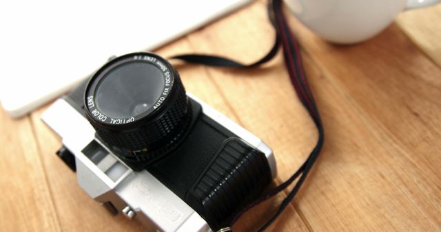 A vintage camera rests on a wooden surface next to a white mug and a notebook, with copy space. The scene suggests a creative or nostalgic setting, belonging to a photography enthusiast or a professional capturing moments on film.