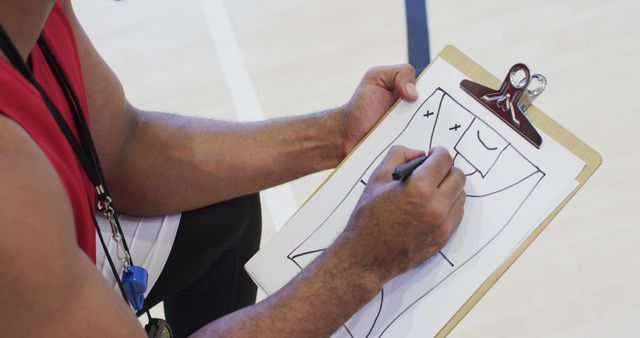 Hands of diverse male coach sketching and advising male basketball team on indoor court. Sport, fitness, health and team sport, unaltered.