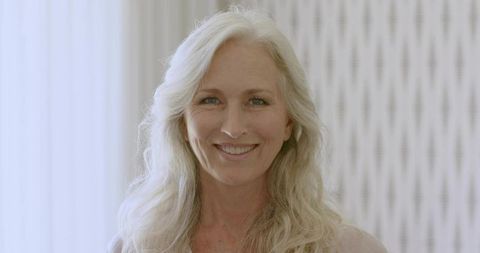 Smiling mature woman with long silver hair facing camera in soft home portrait lighting
