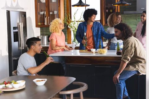 Multiracial friends laughing and chatting over drinks around modern kitchen island counter