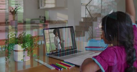 Child raising hand during virtual lesson wearing headset at home study table with laptop