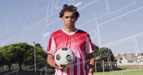 Focused Soccer Player Holding Ball on Grass Pitch Wearing Red and White Jersey