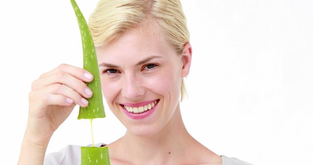 Blonde woman cutting fresh aloe vera leaf, smiling for camera. Aloe gel dripping from leaf. Great for illustrating natural beauty, skincare routines, or organic wellness products. Ideal for health and beauty blogs, articles on natural remedies, or promotional materials for skincare brands.