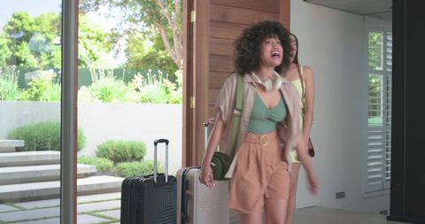 Young diverse friends arriving home with luggage in sunlit modern entryway in beachwear