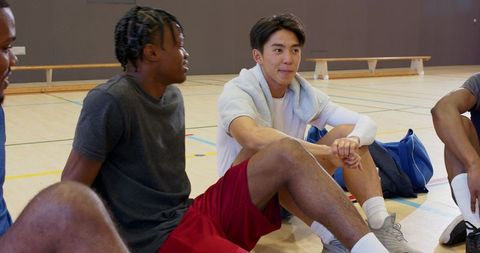 Asian player sitting with teammates talking during break on indoor basketball court