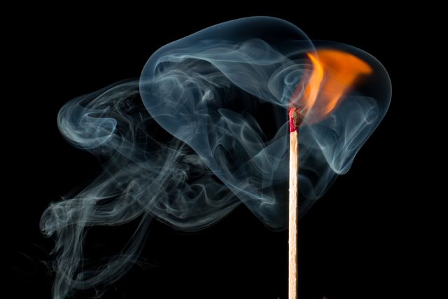 Depicts match igniting with visible smoke trails against black background. Ideal for illustrating themes of ignition, starting, ideas, and heat. Useful in science, safety, and creative design contexts.