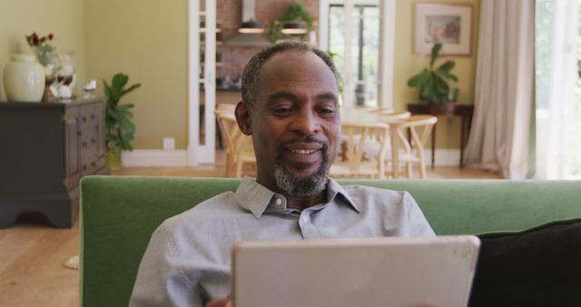 African American man smiling while using tablet in comfortable living room - Download Free Stock Images Pikwizard.com