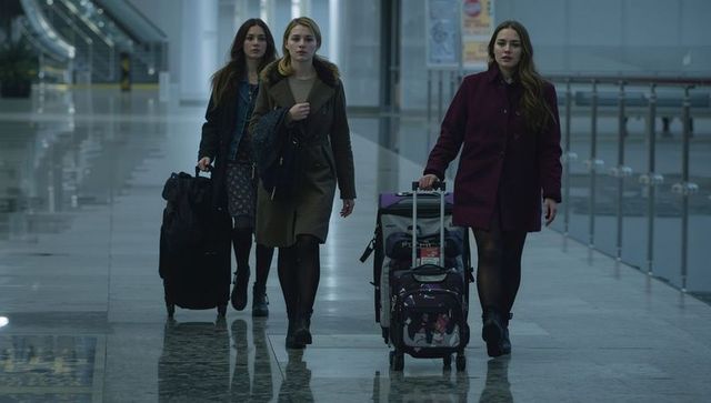 Three young women walking through airport terminal pulling rolling suitcases and luggage