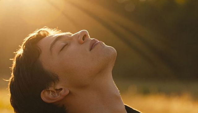 Young man basking in golden hour sunlight with head tilted back, serene profile
